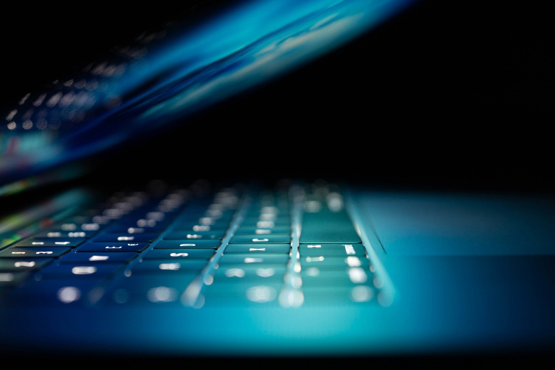 a laptop screen half closed reflecting a blue light onto the keyboard