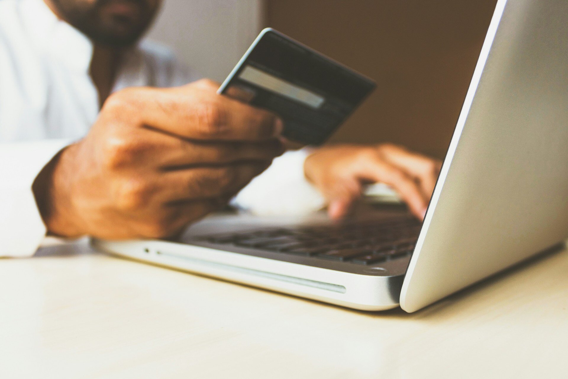 man holding a credit card up in front of a laptop screen for payment